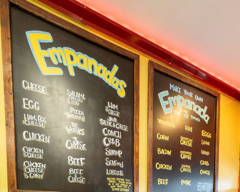 Two chalkboards display a menu of empanada fillings and toppings, including cheese, chicken, and seafood.